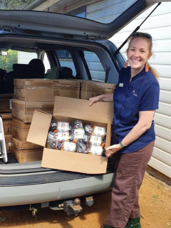 A female school chaplain standing in front of the boot of a car holding a box of donated socks from Hanes.