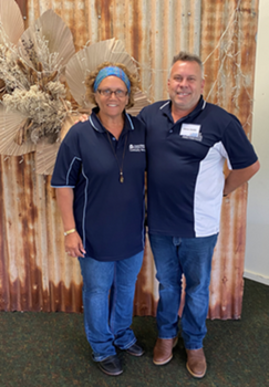 A man and a lady, both dressed in navy shirts and jeans, posing for the camera